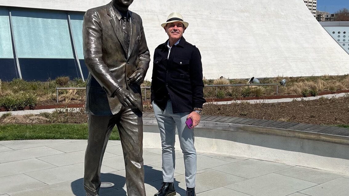 Edwin Fontánez stands next to a statue of President John F. Kennedy walking outside at the Kennedy Center
